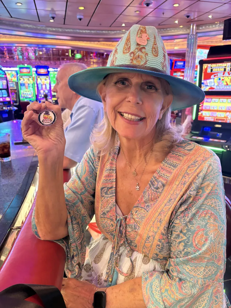 Jackpot Jill in her duck pin hat holds up a lucky duck coin in a ship casino.